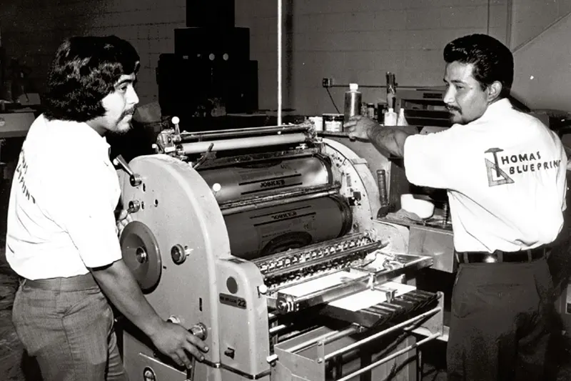 An old photo of two Thomas Blueprint workers operating a machine